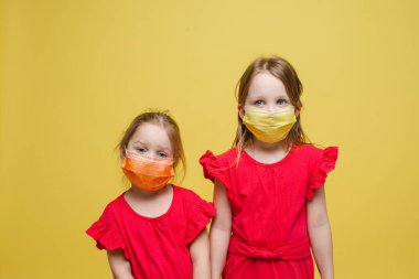 Yüzlerinde tıbbi maske olan iki küçük kızın portresi sağlıklı, kırmızı arka planda izole edilmiş.