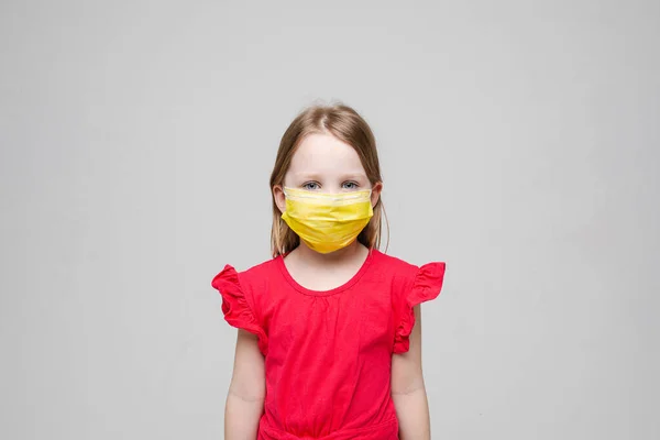 Portret van klein meisje met geel medisch masker op haar gezicht, geïsoleerd op grijze achtergrond — Stockfoto