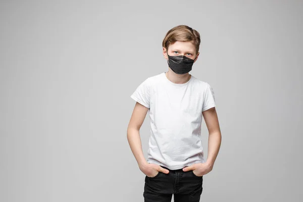 Tiener jongen staat in zwart medisch masker, portret geïsoleerd op grijze achtergrond — Stockfoto