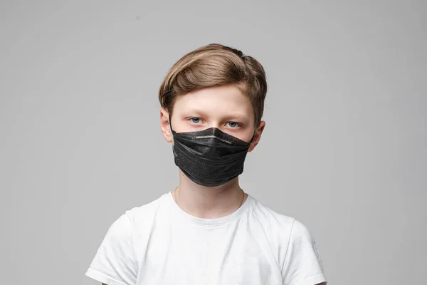 Teenager steht in schwarzer medizinischer Maske, Porträt isoliert auf grauem Hintergrund — Stockfoto