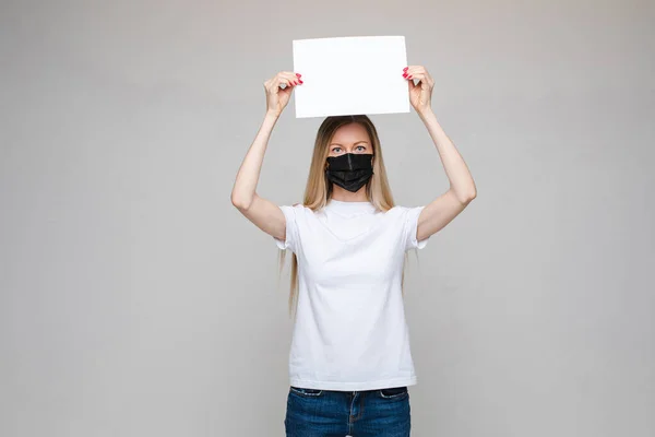 Vrouw met medisch masker poseren met wit vel papier over het hoofd met lege plek voor tekst — Stockfoto