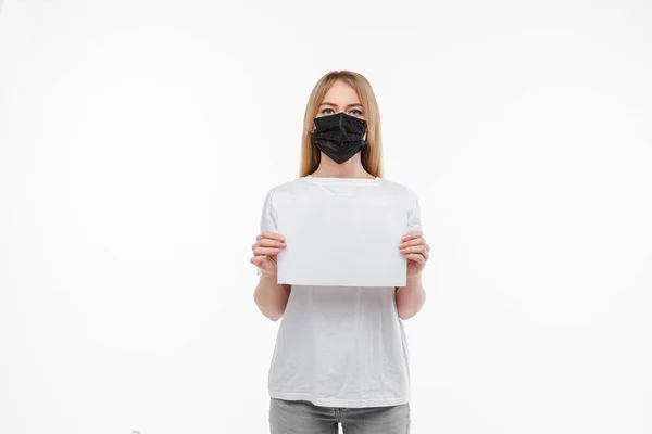 Portret van jonge vrouw met lang blond haar en zwart medisch masker op haar gezicht geïsoleerd op witte achtergrond — Stockfoto
