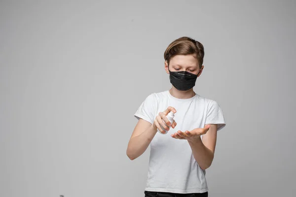 Een jongen met een zwart masker die ontsmettingsmiddel spuit. Stoppen met virussen. — Stockfoto