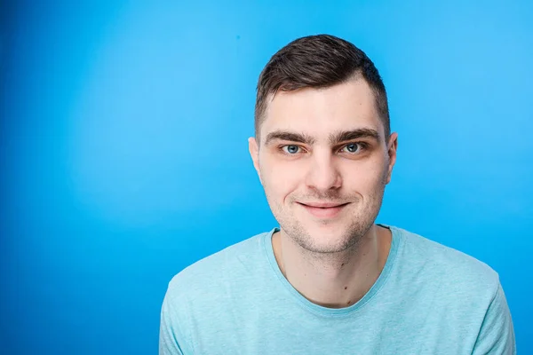 Un giovane uomo in t-shirt blu sorride, immagine isolata su sfondo blu — Foto Stock