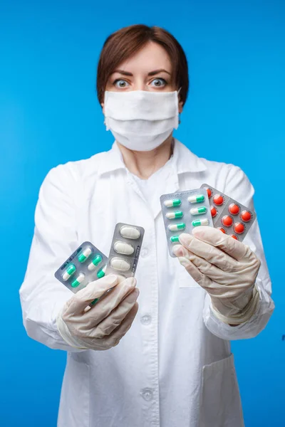 Жінка в масці безпеки тримає різні медичні таблетки, позуючи ізольовані на синьому студійному фоні — стокове фото