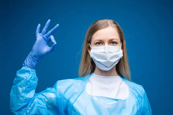 Porträtt av vacker flicka med långt ljust hår med medicinsk mask i ansiktet, bild isolerad på blå bakgrund — Stockfoto
