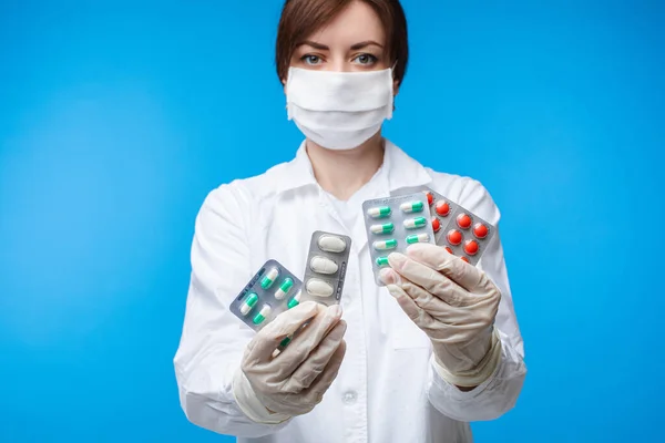 Жінка в масці безпеки тримає різні медичні таблетки, позуючи ізольовані на синьому студійному фоні — стокове фото