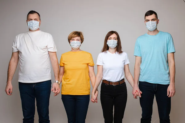 Groep mensen die hand in hand poseren in een medisch veiligheidsmasker geïsoleerd in een witte studio — Stockfoto