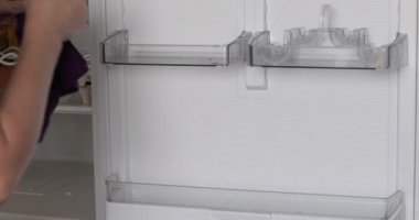 Kadın evdeki buzdolabını yıkıyor.