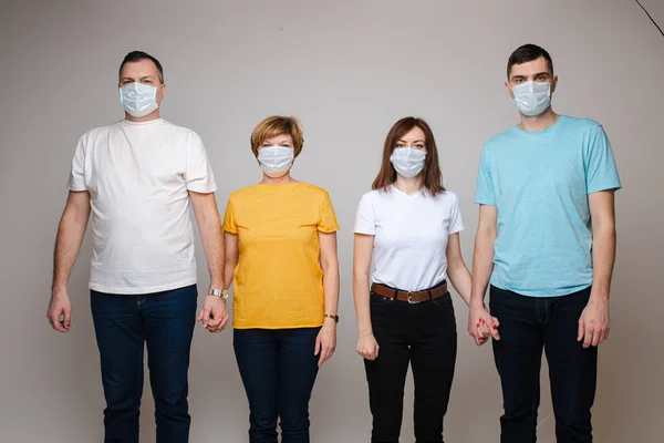 Een familie van vier stands met maskers op hun gezicht en hand in hand, geïsoleerd op grijze achtergrond — Stockfoto