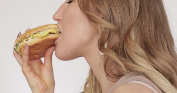 Meisje geniet van haar hamburger in close-up. — Stockvideo