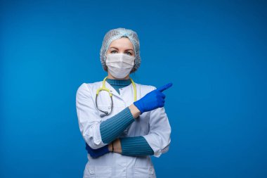Beyaz elbiseli güzel kadın doktor, maske, fonendoskop ve tıbbi şapka, mavi arka planda izole edilmiş resim.