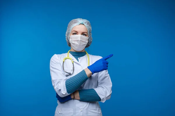 Vacker kvinna läkare i vita medicinska kläder, mask, fonoskop och medicinsk hatt, bild isolerad på blå bakgrund — Stockfoto