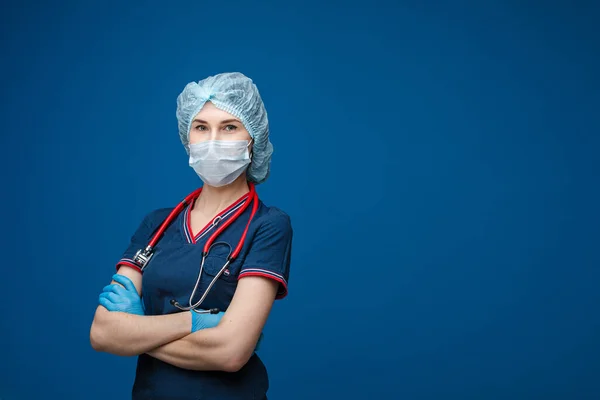 Красива жінка-лікар у білому медичному одязі, масці, фонендоскопі та медичному капелюсі, картина ізольована на синьому фоні — стокове фото