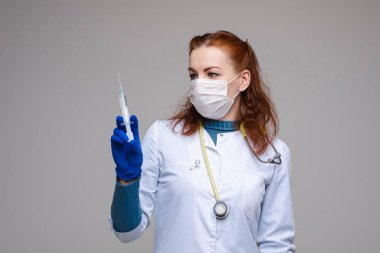 Beyaz elbiseli güzel kadın doktor, maske, mavi eldiven ve omuzlarında fonendoskop, gri arka planda izole edilmiş resim.