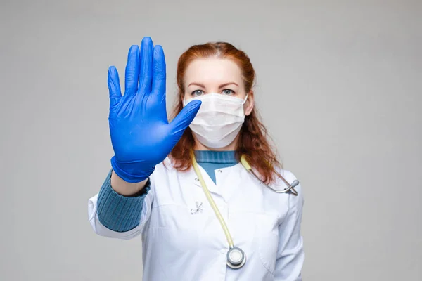 Красива жінка в білому медичному одязі, маска, сині рукавички і фонендоскоп на плечах, картина ізольована на сірому фоні — стокове фото