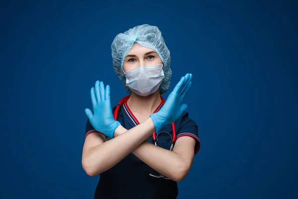 Красива жінка в білому медичному одязі, маска, сині рукавички і фонендоскоп на плечах, картина ізольована на синьому фоні — стокове фото