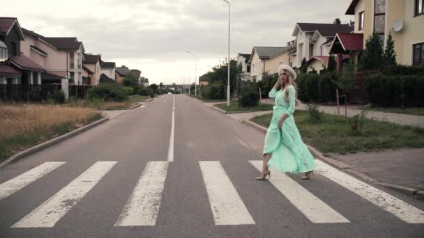 Gyönyörű nő hosszú mentolos ruhában és fehér kalapban sétál az utcán vidéken. — Stock videók