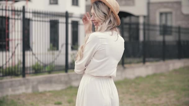 Mujer alegre con hermosos ojos azules grandes, pelo largo y claro, sombrero blanco en vestido blanco rey posa para la cámara y sonríe — Vídeos de Stock