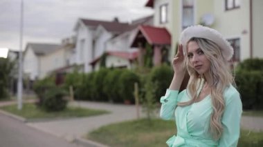 Güzel bir kadın portresi, uzun ve nane rengi elbiseler içinde şapkayı rüzgardan uzak tutar.