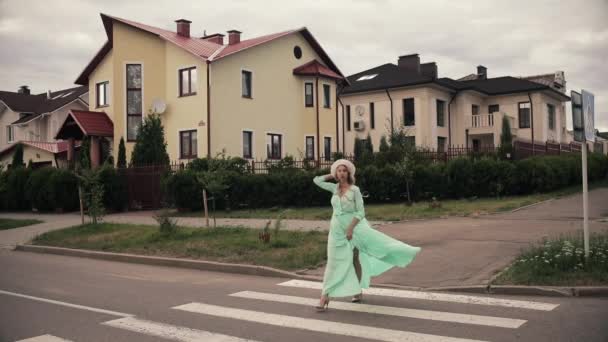 Vacker kvinna i lång mintklänning och med vit hatt promenader på gatan på landet — Stockvideo