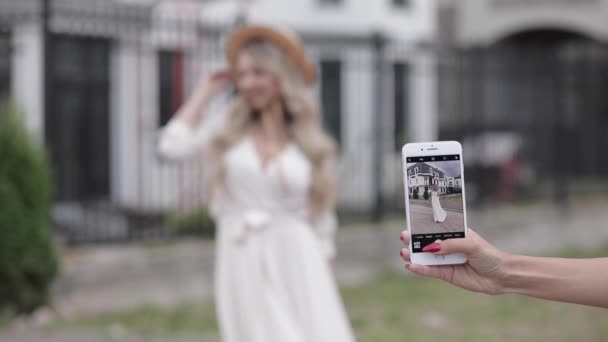 Brazo con smartphone tomando fotos de una mujer en vestido . — Vídeo de stock