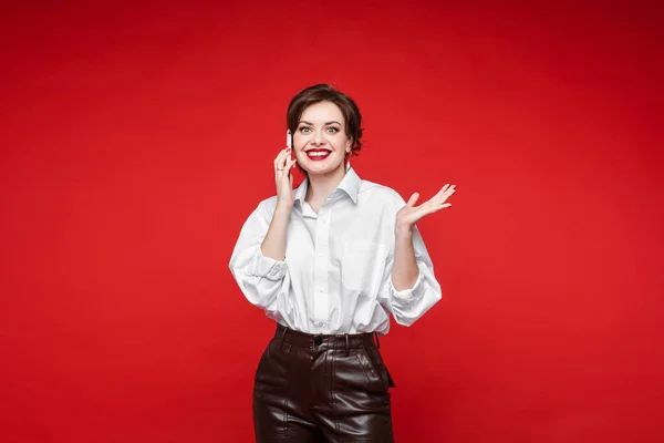 Schöne junge Frau spricht mit ihrem Freund mit einem Handy und lächelt, Bild isoliert auf rotem Hintergrund — Stockfoto