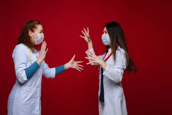 Porträtt av två kvinnliga läkare i medicinska kläder med fonendoskop runt halsen argumenterar, bild isolerad på röd bakgrund — Stockfoto