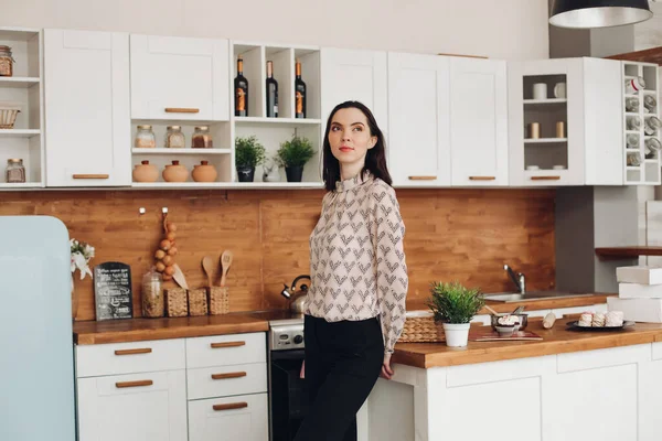 Mutfakta duran güzel esmer. Modern mutfakta dikilip düşünceli bakışlar atan desenli bluz, siyah pantolon ya da kot pantolon...