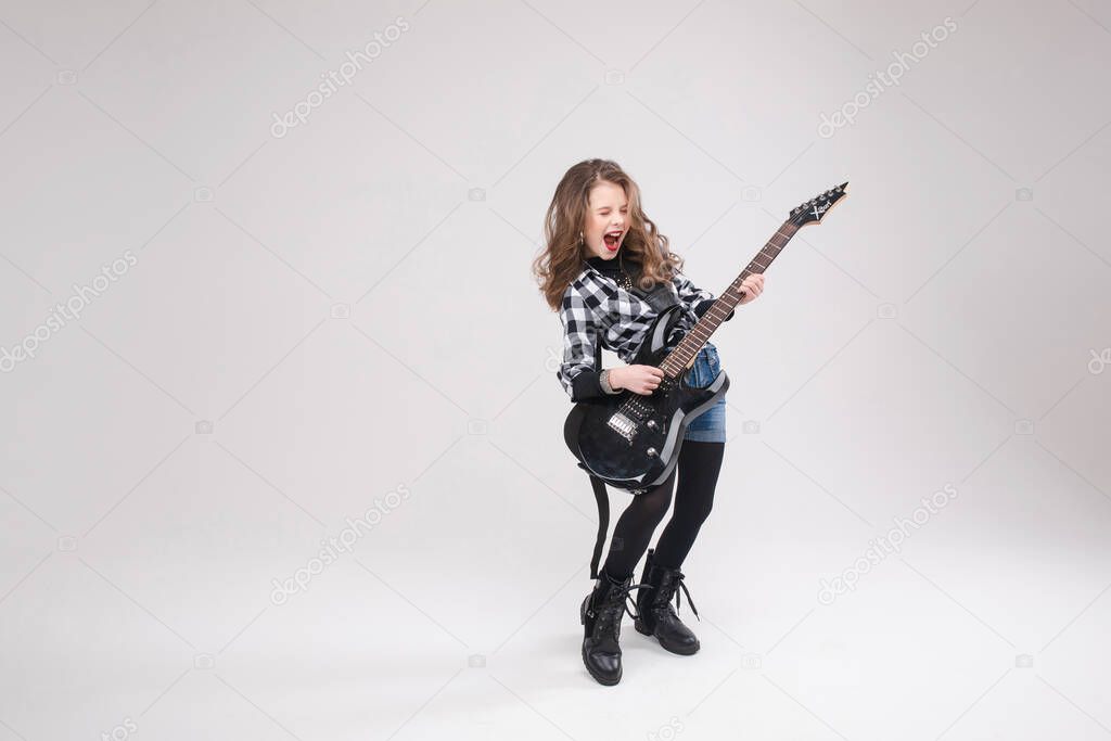 Happy beautiful artistic small girl playing guitar in studio