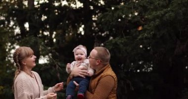 Sevgi dolu anne kızını babasının elleriyle parkta öpüyor..