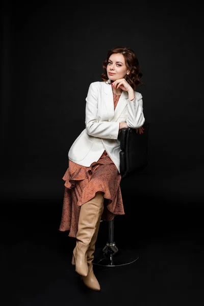 Retrato de mulher bonita em vestido longo e botas senta-se em um chait e posa para a câmera, imagem isolada no fundo preto — Fotografia de Stock