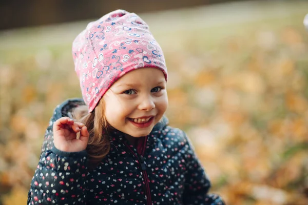 Söt liten flicka i tryckt hatt ler mot kameran. — Stockfoto