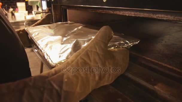 Taking hot tray covered in aluminium paper out of an industrial oven — Stock Video