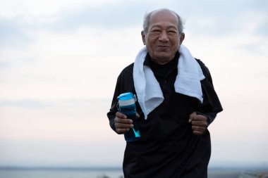 Asyalı ihtiyarlar mutlu bir gülümseme sergiliyor. Son sınıf öğrencisi elinde su şişesiyle sabah güneşinde yolda koşuyor. sağlık yaşam tarzı ve egzersiz kavramı.