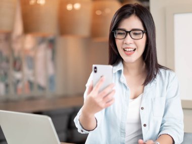 Asyalı bir kadın, evdeki video görüşmesi için akıllı telefonu kullanmaktan mutlu. Teknoloji, Yaşam Tarzları ve İletişim