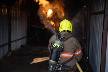 İtfaiyecinin arkadan görünüşü yangın koruma giysisi giyip yangın söndürme odasına giriyor ve itfaiye istasyonunda su püskürtüyor. Eğitim yangın tatbikatı.