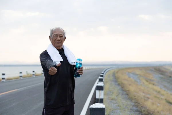 Asian Senior man in exercise clothes holding water bottle and many thumbs up. Concept Health care, Healthy with exercise and Healthy good start.