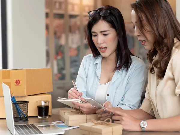 Two brothers owener of small family business. Woman check orders with Smart Phone, Laptop and packing product in boxes, preparing it for delivery. online seller business work from home.