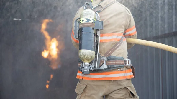 消防士の後方ビューは消防訓練室と消防署でスプレー水火災に歩いて防火スーツを着用してください 消防訓練の概念 — ストック写真