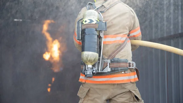 Rear view of Fireman wear fire protection suit walking into the fire training room and Spray water Fire at fire station. Training fire drill Concept.