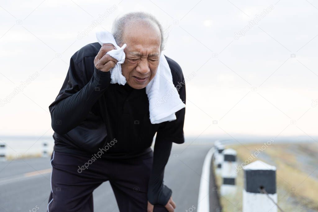 Close up Asian elderly wiping sweat with towel after exercised running on road in the morning sunshine. health lifestyle and exercise Concept.