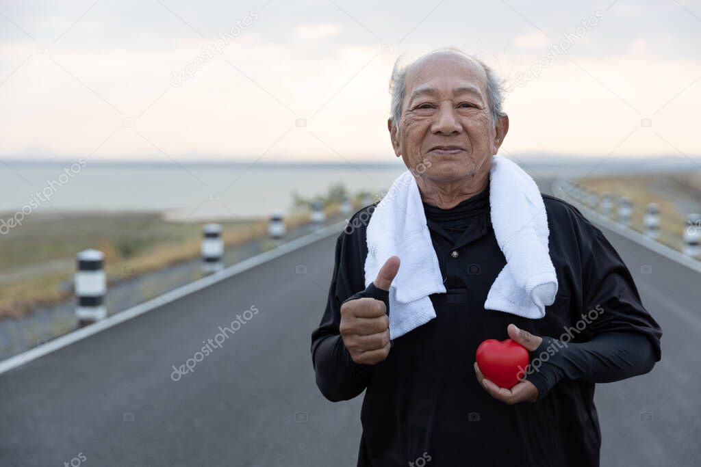 Asian Senior man in exercise clothes holding red heart and many thumbs up. Concept Health care, Healthy with exercise and Healthy good start, insurance, world heart day, Medical insurance
