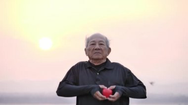 Son sınıf öğrencisi, elinde kırmızı bir kalple ve mutlu bir gülümsemeyle sabahları güneşin doğuşuyla. Sağlık, egzersiz ve sağlıklı başlangıç, sigorta, dünya kalp günü, sağlık sigortası.