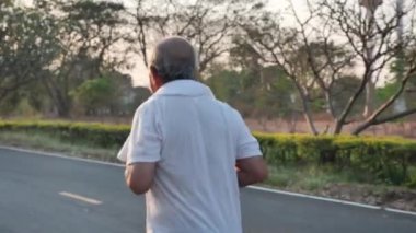 Arkadan bakıldığında Asyalı yaşlılar egzersizi. Kamu parkında akşam güneşli yolda koşan kıdemli bir adam. Sağlık yaşam tarzı ve egzersiz konsepti. Yavaş Hareket