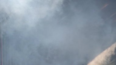 Axe 'a güvenen Asyalı itfaiyeci arka planda yanan ateşle dumanın içinden geçiyor. İtfaiyeci kariyeri, eğitim yangın tatbikatı konsepti. Yavaş çekim.