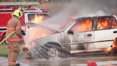 Asyalı itfaiyeci yangın koruma giysisi giyiyor. İtfaiyeci yangın tatbikatı sırasında itfaiye arabasında ateşle savaşıyor. İtfaiye istasyonunda trafik kazası, itfaiyeci kariyeri kavramı. Yavaş çekim