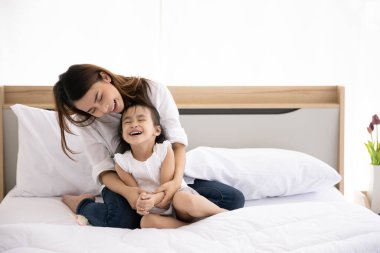 Mutlu Asyalı aile. Üç yaşındaki bekar anne ve kız çocuk pencereden gelen güneş ışığıyla evin yatağında birlikte oynuyorlar..