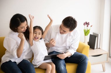 Mutlu Asyalı aile teknolojileri eğlence için kullanıyor. Baba, anne ve kız evdeki kanepede dijital tablete bakıyor. İletişim teknolojisi ve yaşam tarzı