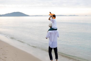 Mutlu Asyalı Aile Yaz Tatili Oğlu Baba 'nın omuzlarında birlikte uçak uçurmaca oynuyorlar Sabah vakti kumsalda yürüyorlar, gün doğumunda. Tatil ve Seyahat kavramı.